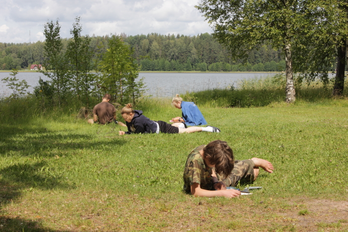 Noored on kõhuli ja istuvad ning joonistavad tähelepanelikult loodust järve ääres