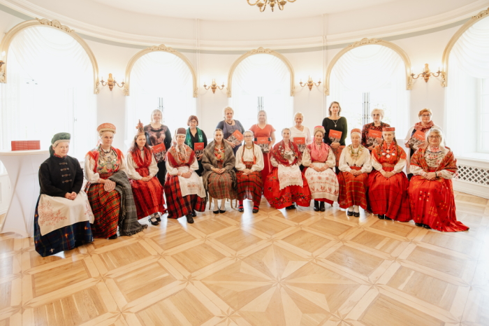 punasekirjudes pildulikes rõivastes naised istumas valgusküllases kõrgete lagedega ruumis