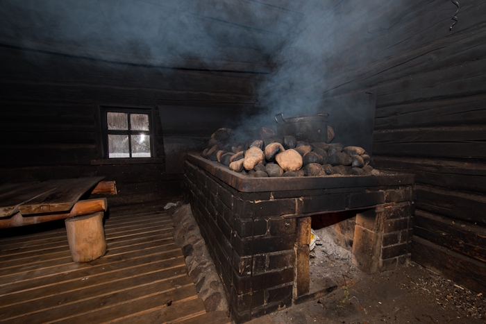tumedate tahmunud seintega puidust sauna leiliruum koos suure kerisega, millel kivide khalt tõuseb suitsu