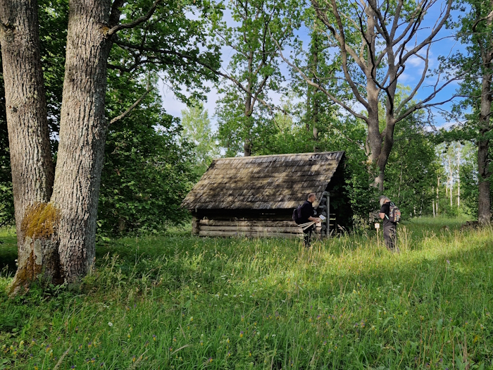 üksikute puudega niiduala, taga küün. Inimesed panevad üles silte
