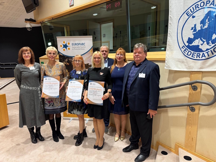 seitse pidulikult riietatud inimest seisavad, Europarc Federation lipu juures, sertifikaadid käes